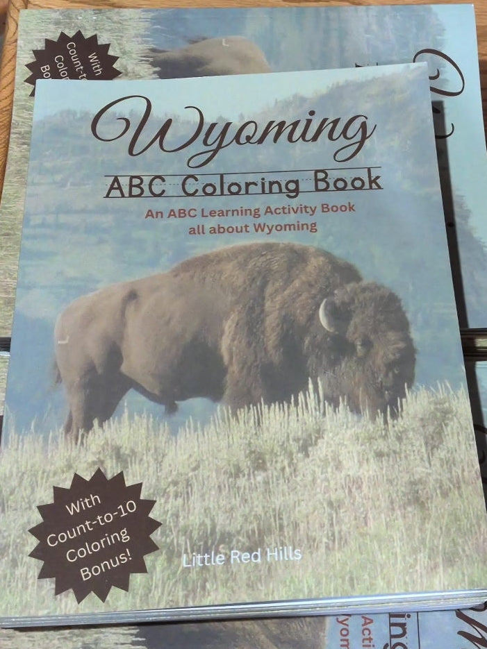 Wyoming ABC Coloring Book on a wooden table with a candle and other items.